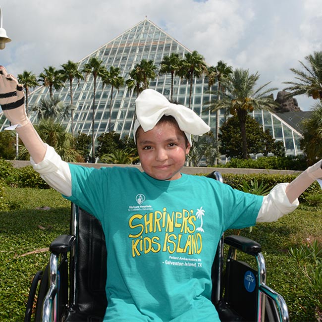 Patient in wheelchair wearing "Shriners Kid Island" shirt